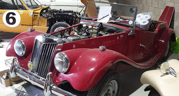 a red classic car with its engine exposed in HRClassics' workshop